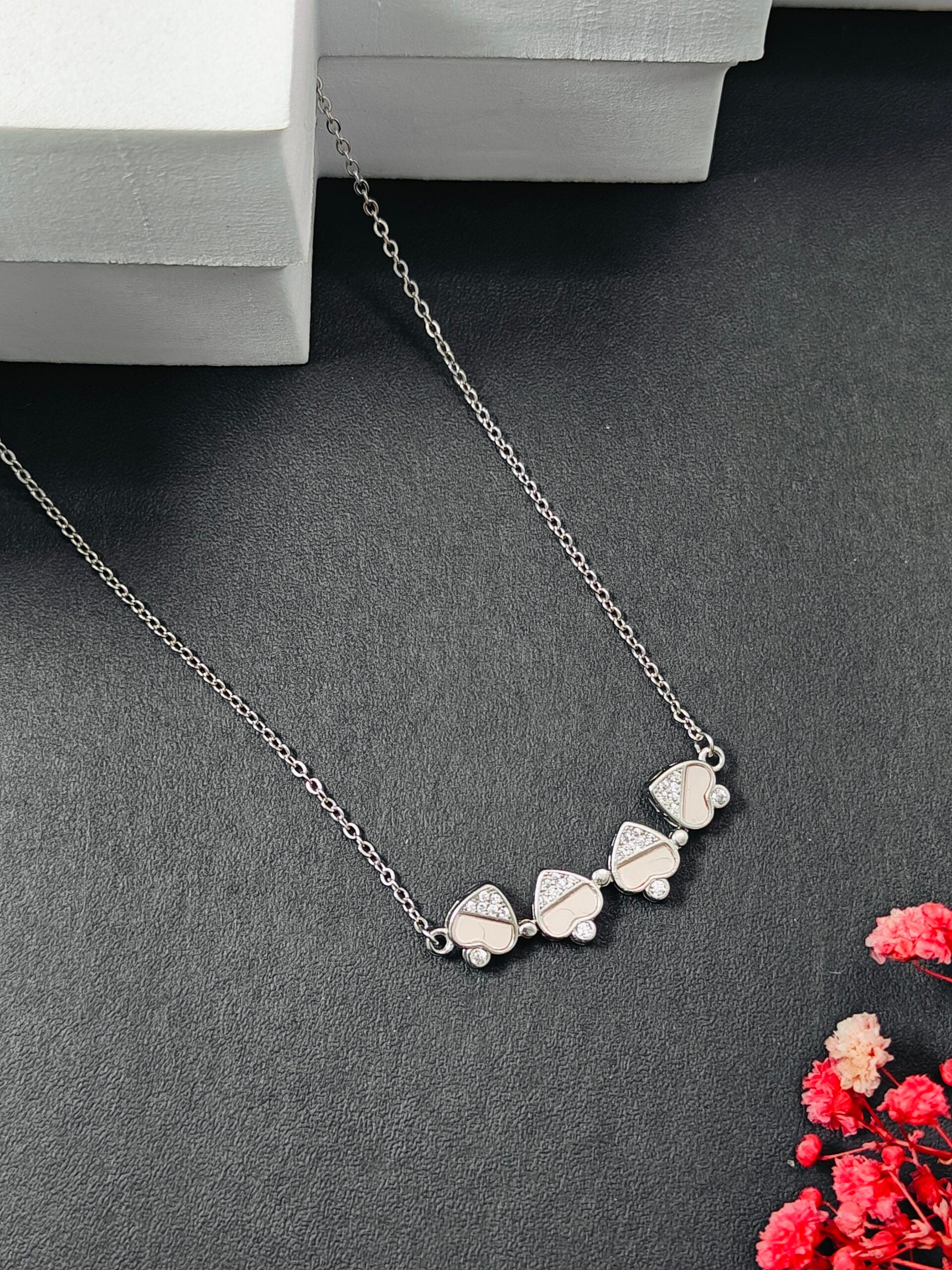 Silver necklace with floral pendants on a dark surface with red flowers.